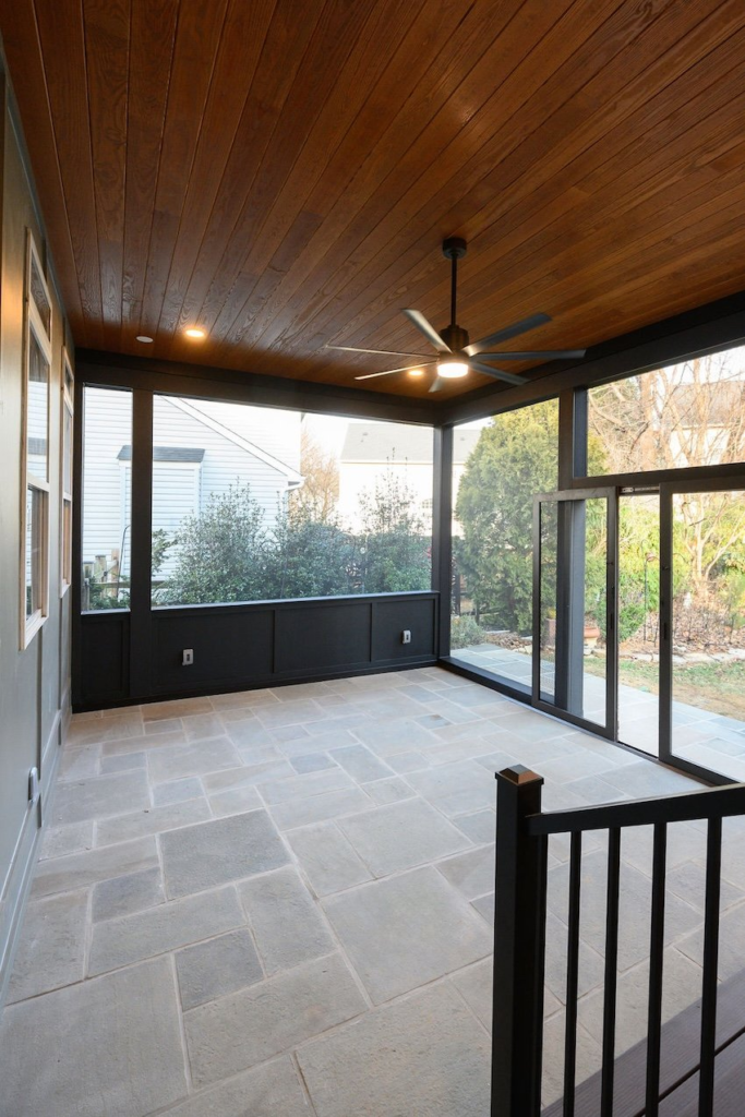 Custom screened porch interior in Columbia, MD featuring stone flooring, dark wrapped beams, and a stained pine ceiling.